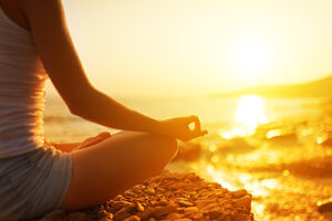 woman meditating on a beach enjoying Holistic Therapy