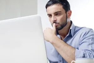 A man sitting at a desk looking concerned while staring at a computer.