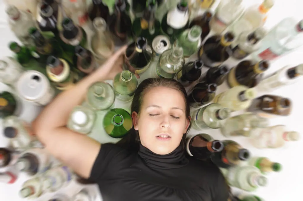 A woman lying down, surrounded by a swirling circle of empty glass bottles.