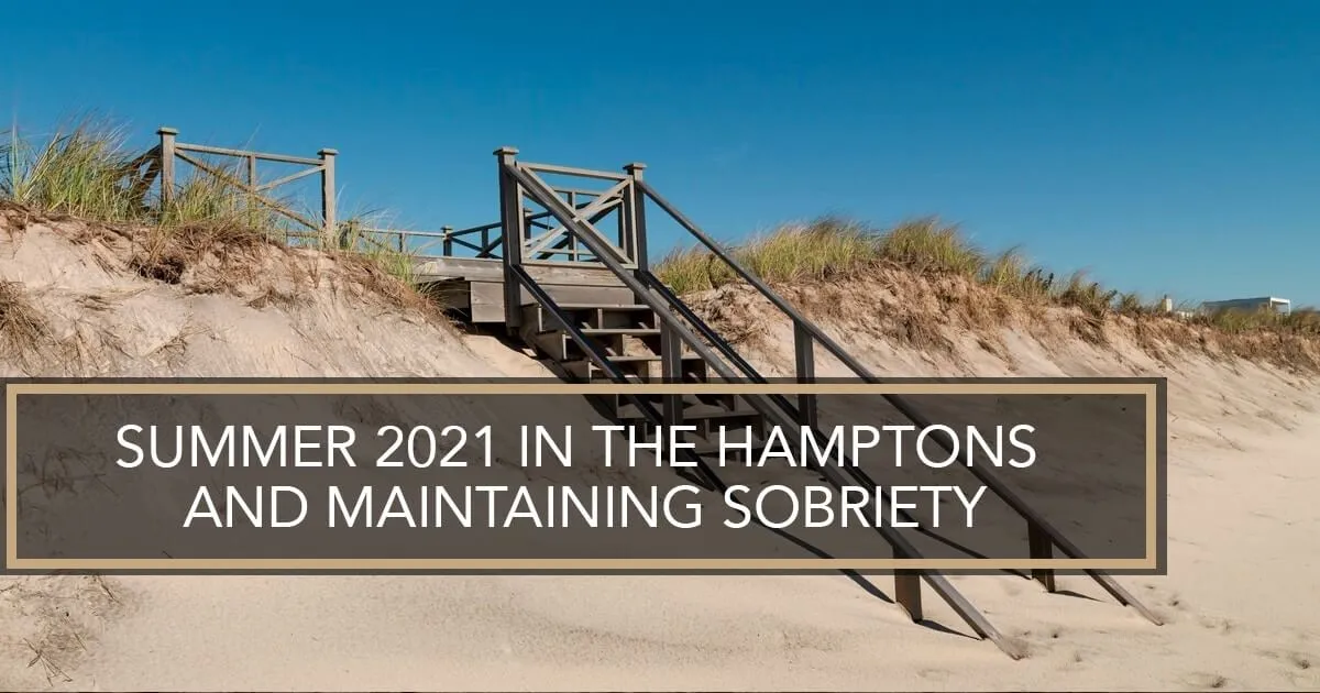 A wooden staircase leading over a sand dune with beach grass under a clear blue sky.