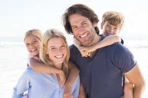 A portrait of a smiling family of four on a sunny beach.