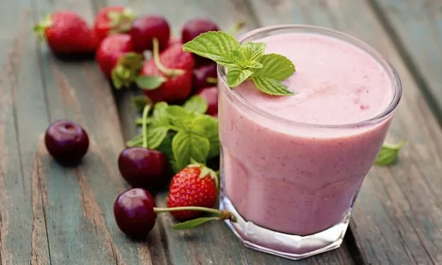 A glass of thick, pink berry smoothie garnished with fresh mint leaves sits on a rustic wooden surface.