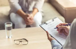 Therapist writing on a clipboard during a session with a blurred patient.