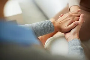 One person's hands gently holding and comforting another person's hands in a gesture of support and empathy.