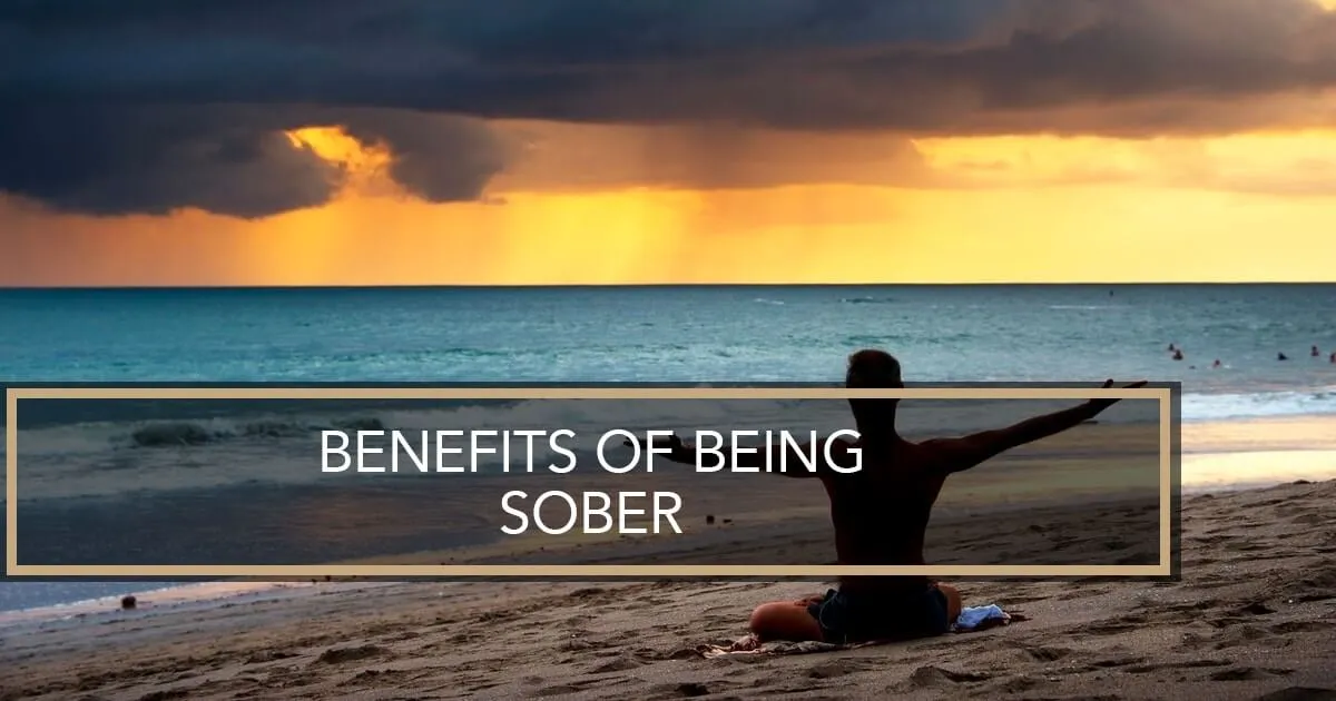 A person sitting in a meditative pose on a beach at sunset, with their arms outstretched toward the ocean.