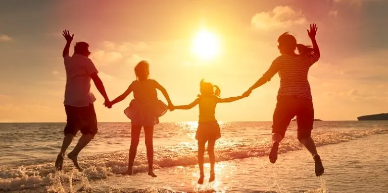 A silhouette of a family jumping for joy while holding hands on a beach at sunset.