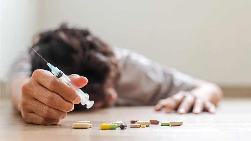 Unconscious drug addict hands lying on grungy concrete floor with pills, syringe, cooked heroine.