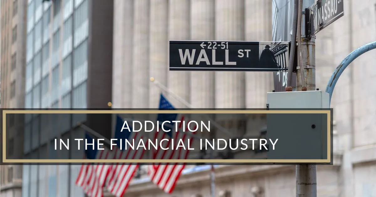 A street sign for Wall St is attached to a pole in front of a large building with American flags.